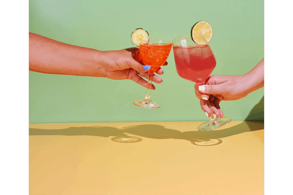wo people cheersing with colorful cocktails garnished with lime and cucumber against a vibrant green and yellow backdrop, celebrating Founding Spirits' fresh, award-winning gin creations.